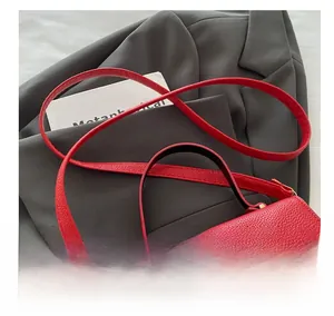 Gros plan sur le sac en cuir rouge avec boucle métallique SM et bandoulière assortie