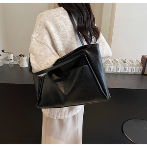 Detail view of large black tote bag with side pocket shown in cozy cafe setting