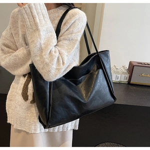 Detail of minimalist black leather tote bag with large front pocket and slim handles