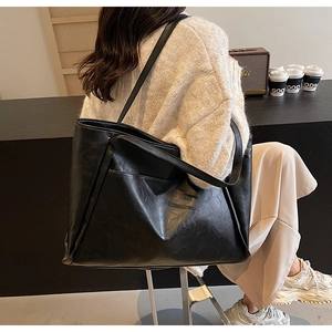 Close-up of a large black vintage leather tote bag worn by a model in a cozy cafe setting
