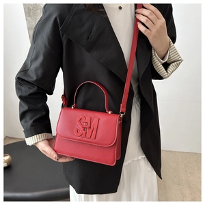 Détail d'un sac à main rouge en cuir grainé avec finitions dorées et logo embossé