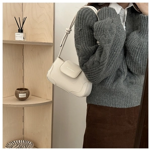 Detail of cream leather shoulder bag featuring minimalist flap and knotted strap design