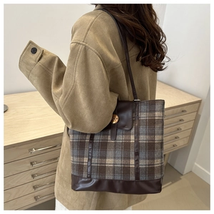 Detail of checkered tote bag with brown leather trim and golden N-engraved buckle