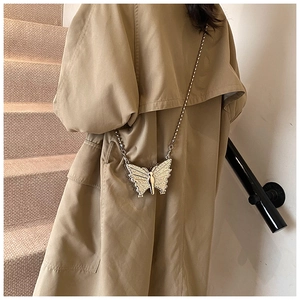 Detailed view of butterfly-shaped silver mini bag with beaded chain on trench coat
