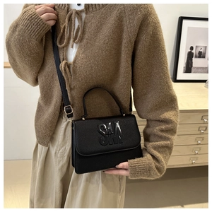 Détail d'un sac à main noir en cuir grainé avec un logo SM métallique brillant décoratif