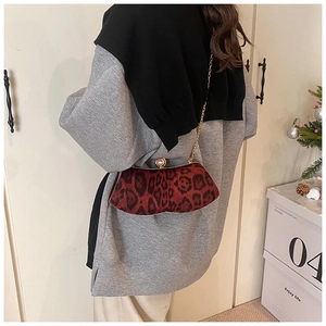 Détail du sac bandoulière léopard rouge avec chaîne dorée et fermoir perle porté par mannequin