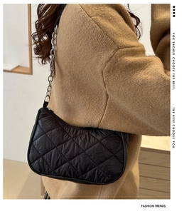 Detail of black quilted baguette bag with diamond pattern and silver chain strap