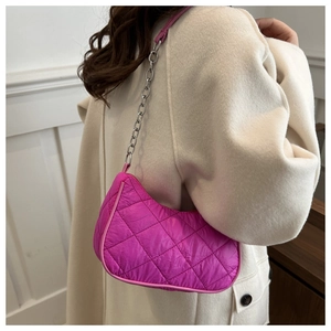 Detail of fuchsia quilted crescent shoulder bag with silver chain strap on white coat