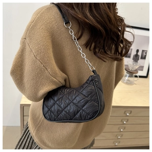 Detail of black quilted shoulder bag with silver chain strap worn by a model