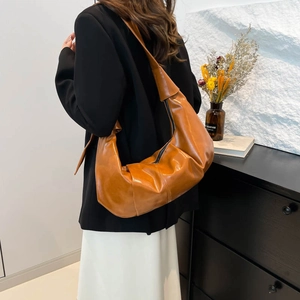 Caramel glossy leather crescent shoulder bag with pleated texture worn by model