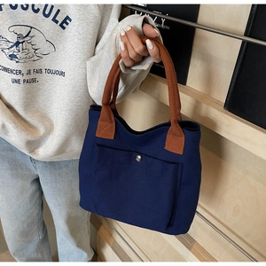Détail du sac à main en toile bleu marine avec anses marron et fermoir à bouton pression