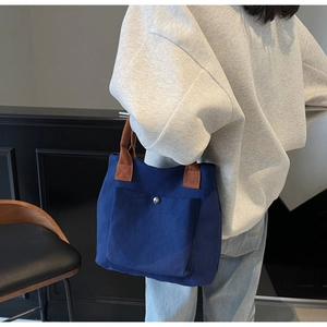 Detail of dark blue canvas tote bag featuring brown straps and a metal snap front pocket