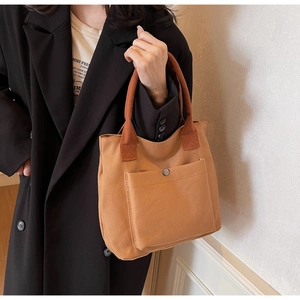 Brown canvas tote bag with contrast handles and front pocket detail held by a model