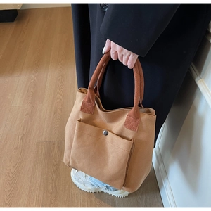 Detail view of khaki canvas tote with brown straps and silver metal snap pocket
