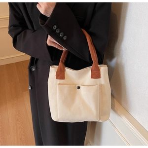 Detail of canvas tote bag with brown straps and metal snap button on front pocket
