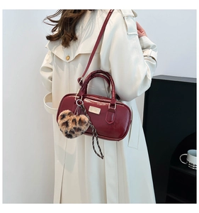 Detalle de bolso de cuero brillante burdeos con dije de corazón de leopardo y cinta en gabardina