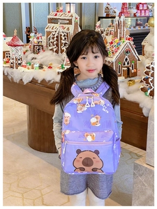 Toddler modeling purple capybara backpack in a festive gingerbread house setting