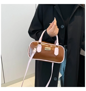 Detalle de bolso cilíndrico marrón y rosa con placa dorada y correa ajustable