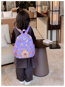 Child wearing purple cartoon Capybara backpack in a cozy indoor setting, back view