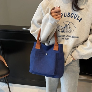 Minimalist navy canvas tote bag with brown handles and a front snap pocket for daily use