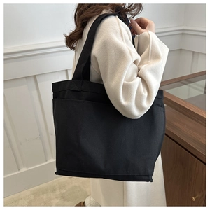 Detail of a large black canvas tote bag showing the side view and wide shoulder strap