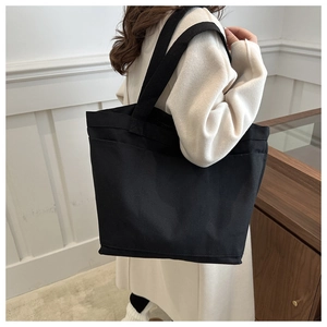 Side view of a minimalist black canvas tote bag with double handles shown on a model