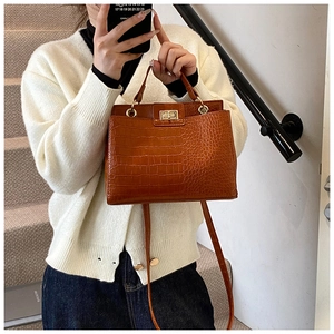 Detail of brown croc-effect tote bag with gold hardware shown on a model on stairs