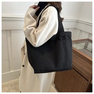 Detail view of large black canvas tote bag with front pockets on a model shoulder