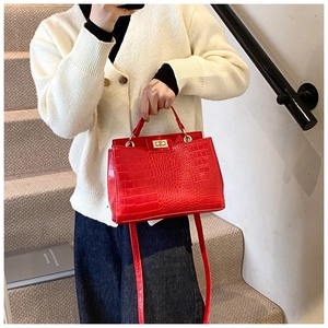 Detail of red crocodile pattern handbag featuring a gold twist lock and round handle