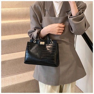 Detail of black faux crocodile skin texture and gold metal twist lock on a tote bag