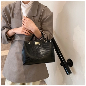 Close-up of black croc-embossed tote bag with gold rectangular twist lock and top handle