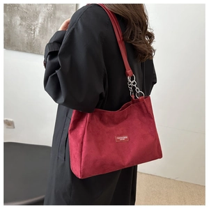 Detail of red suede tote bag with leather metal chain strap on model shoulder