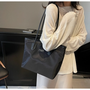 Side view of large black nylon tote bag on shoulder showing fashion tag and spacious design