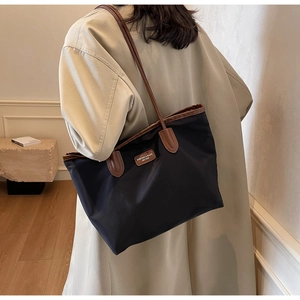 Detailed view of spacious nylon tote bag with leather trim on model in trench coat