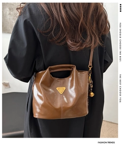 Detalle de bolso tote marrón brillante con logo de triángulo dorado y colgante de bola
