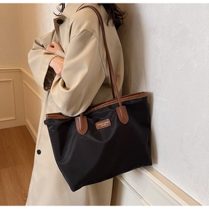 Detail of black nylon tote bag with brown leather handles and brand label on front