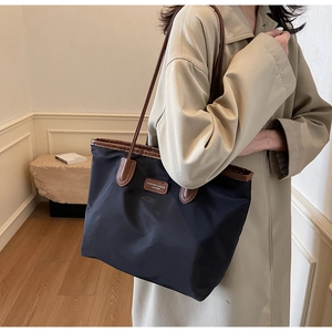 Close-up of black nylon tote bag with brown leather handles on a minimalist background
