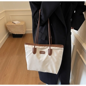 Detail of minimalist cream nylon tote with brown leather handles worn on the shoulder