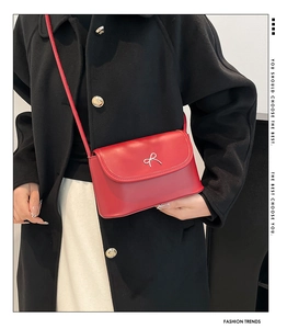 Detail of red leather crossbody bag featuring a decorative silver metal bow buckle