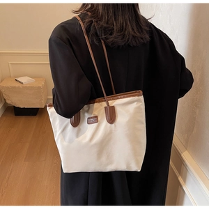 Detail of a large cream nylon tote bag with contrasting brown leather handles and brand tag