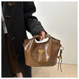 Detalle de bolso de cuero brillante marrón oscuro con logo de metal dorado