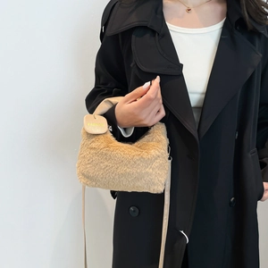 Elegant beige plush handbag with leather handle and fashion tag worn on a black coat