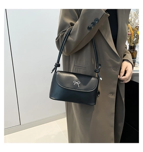 Detail of black leather shoulder bag with silver bow ornament and knotted strap design