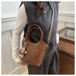 Detail view of a vintage brown bucket bag with plush charm and adjustable strap