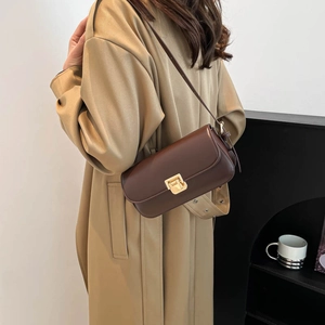 Sac à bandoulière carré marron foncé classique avec boucle dorée porté sur un trench-coat