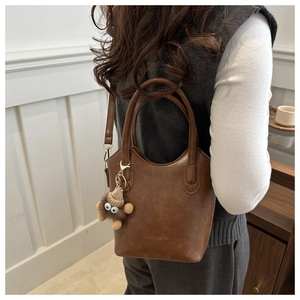 Detailed shot of a vintage brown PU leather bucket bag with a cute plush monster charm
