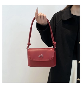 Detail of red synthetic leather crossbody bag featuring a silver metal bow buckle