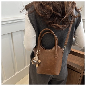 Detail of retro dark brown leather bucket bag with top handles and plush monster charm