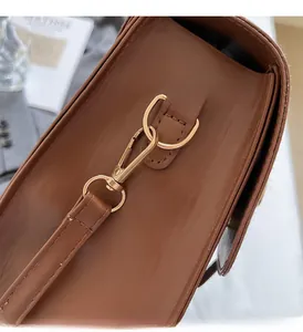 Detailed close-up of brown leather bag with polished light gold metal hardware and stitching