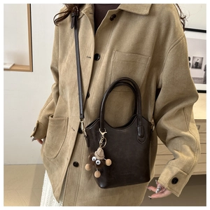 Detail of dark brown leather bucket bag with top handle and plush monster charm